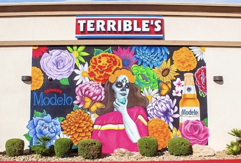 terrible art mural with a floral background and a woman with sugar skull face paint and a modelo bottle